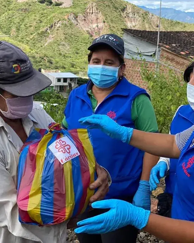 Dos voluntarias entregan un paquete de mercado a un hombre en una vereda